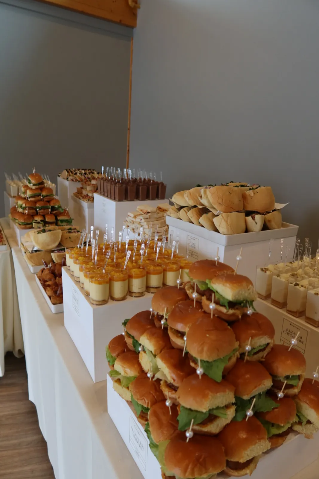 Indian-fusion grazing table with stacked sliders and dessert cups on white risers at a wedding lunch at Azuridge Estate Hotel in Priddis, by Deep's Delights