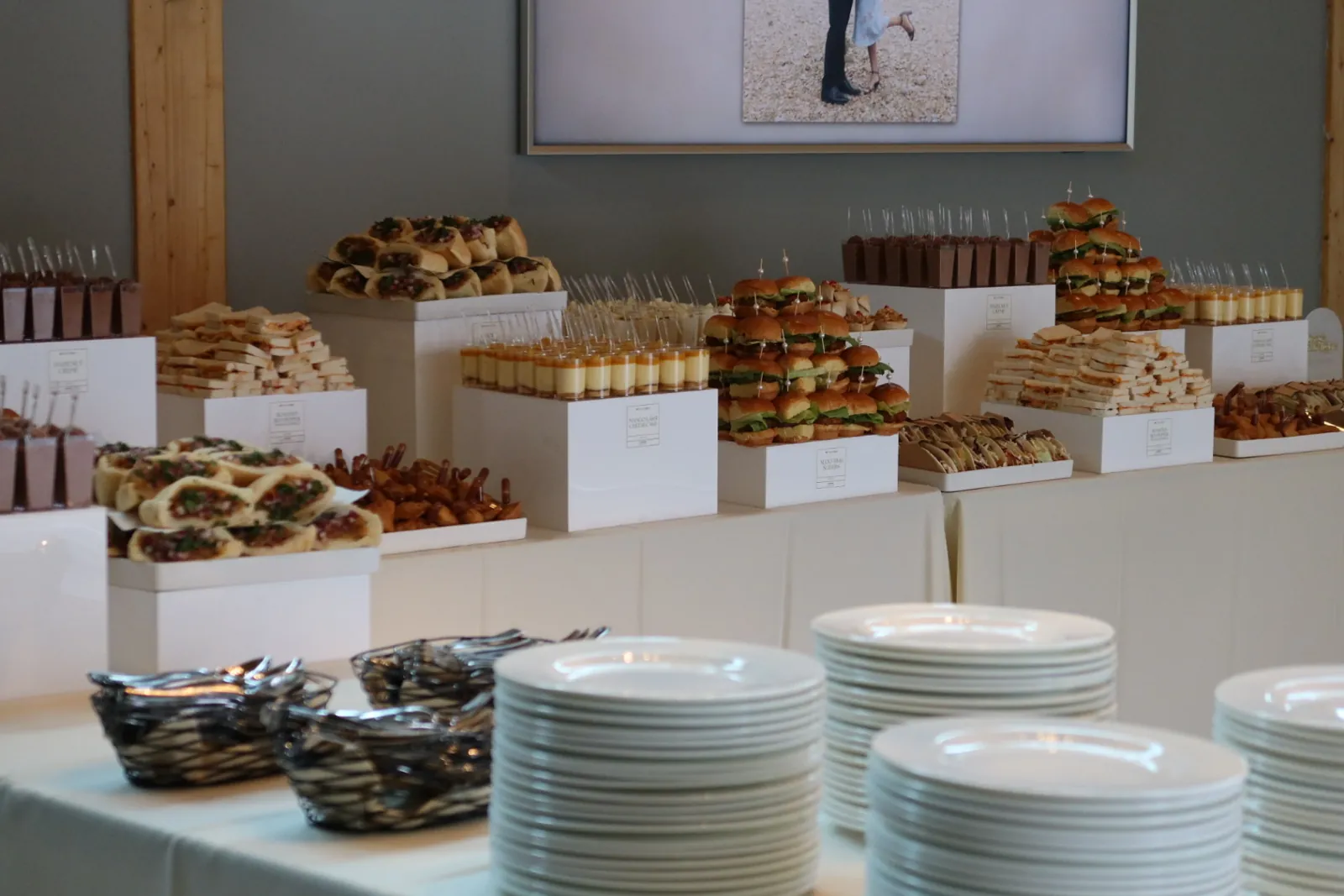 A long grazing table of Indian-fusion sliders, samosas and dessert cups on white risers, styled by Deep's Delights, Calgary caterers