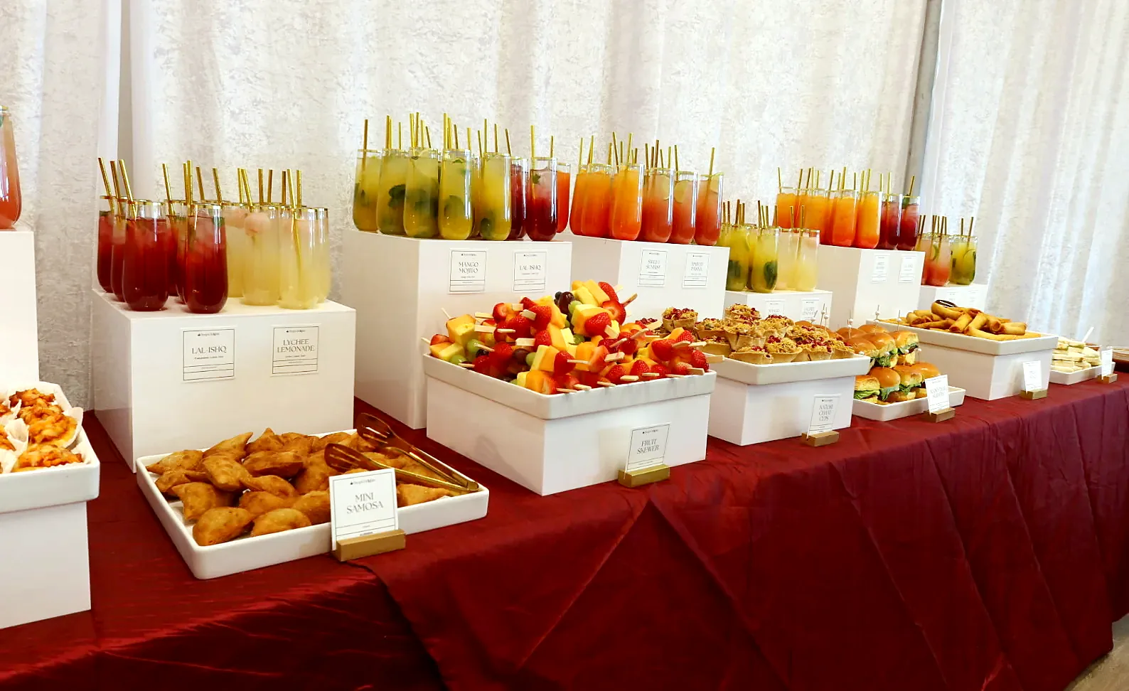 A row of colourful poured mocktails beside an appetizer display on burgundy linen in a Calgary banquet hall