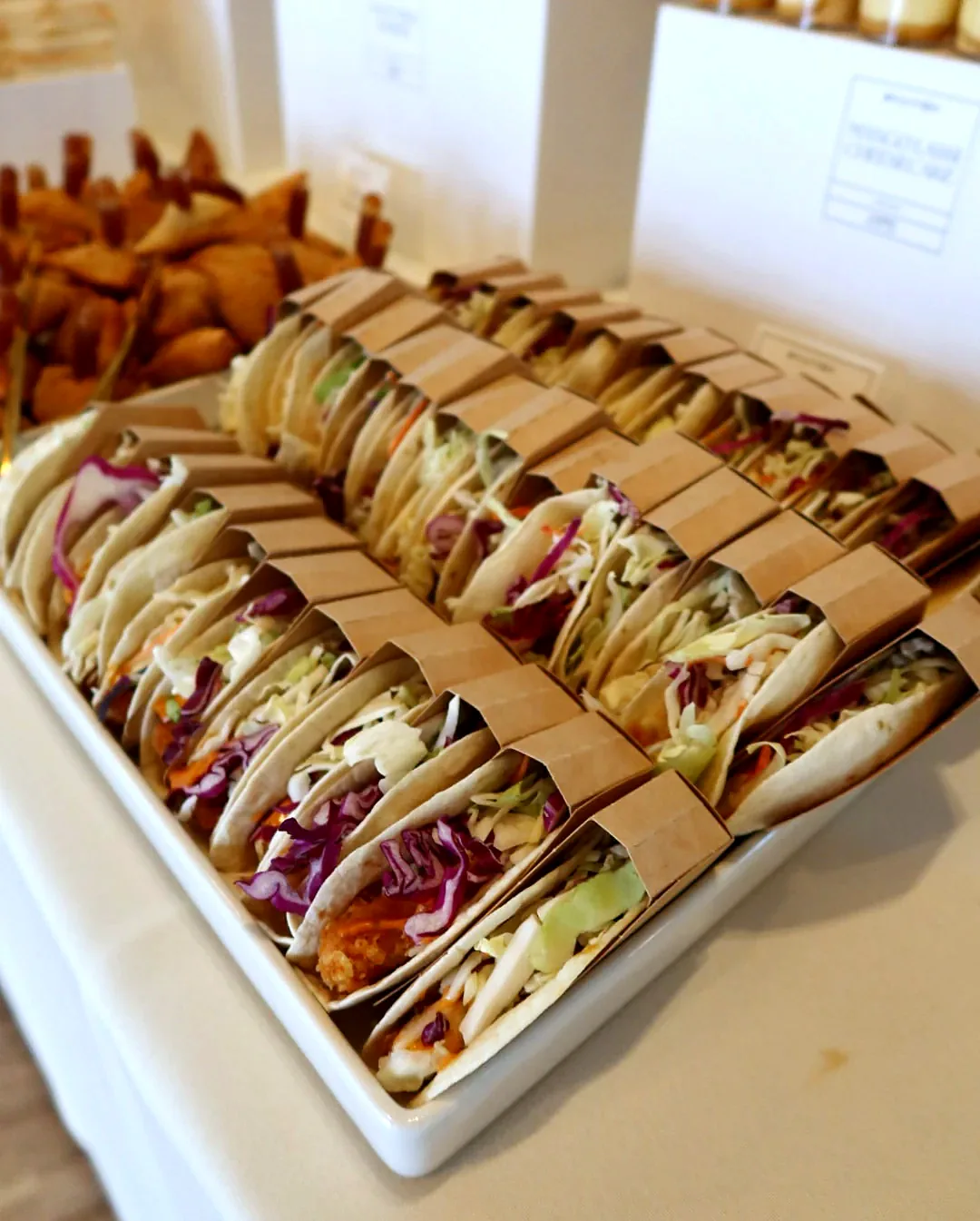 Paneer tacos in kraft paper sleeves lined up on a white platter