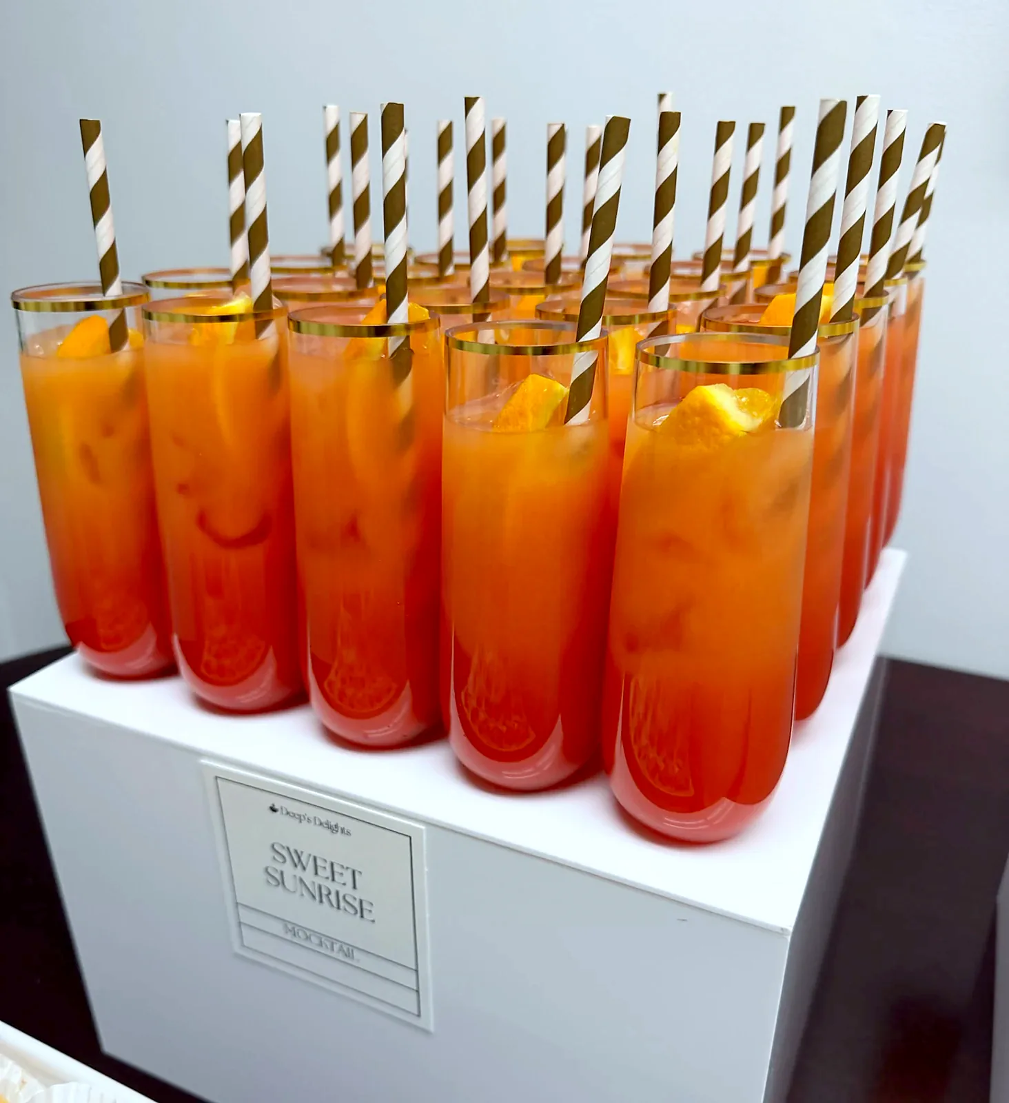 Sweet Sunrise mocktails with striped paper straws on a white display cube, styled by Deep's Delights